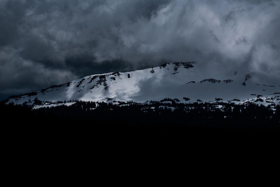 Free Image of A snow-covered mountain under dark, stormy clouds 