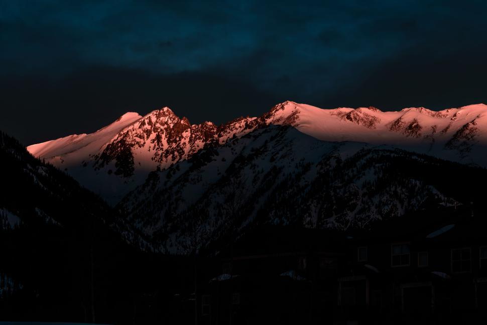 Free Image of Sunlit mountain peaks with snow in dramatic twilight sky. 