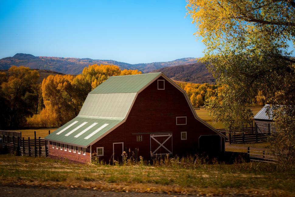 Free Image of Rustic red barn amidst autumnal landscape and trees 