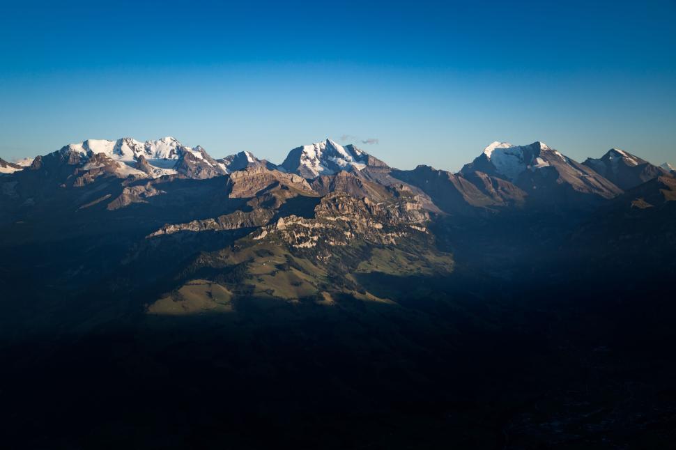 Free Image of Mountain range under a clear blue sky with shadowed valleys 