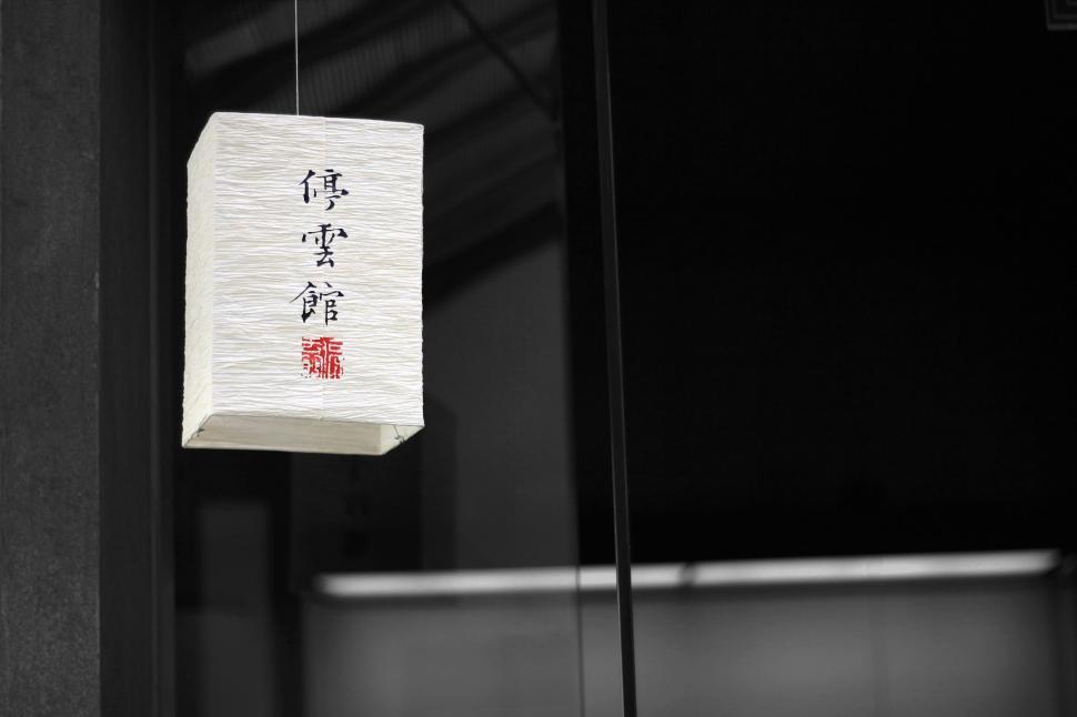 Free Image of Illuminated lantern with foreign script hanging in darkened setting. 
