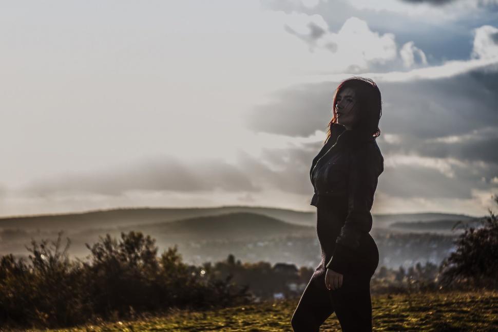 Free Image of Silhouette of a woman standing on a hill overlooking sunset vista 