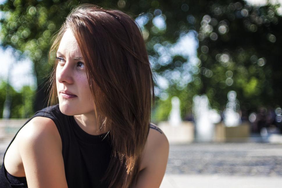 Free Image of A young woman in a park, looking thoughtfully to the side 