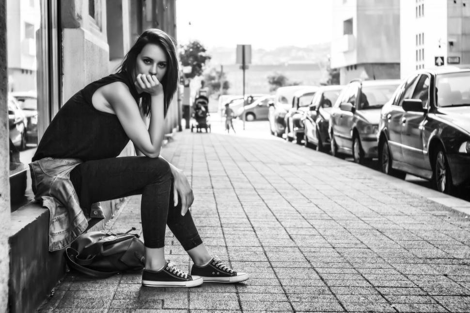 Free Image of Black and white image of a woman sitting on a sidewalk 
