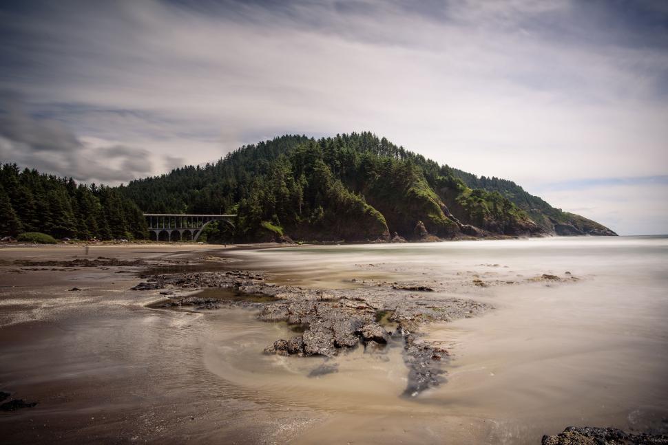 Free Image of Scenic coastal landscape with bridge and lush green hill. 