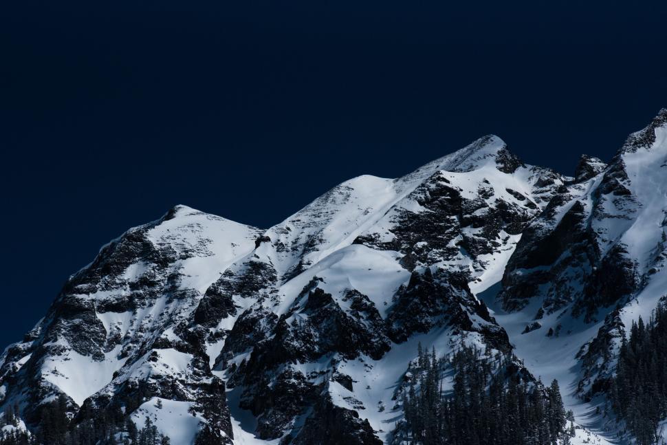 Free Image of Snow-covered mountain peaks against a dark, deep blue sky. 