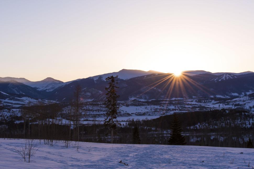 Free Image of Sunrise over snowy landscape with mountain backdrop. 