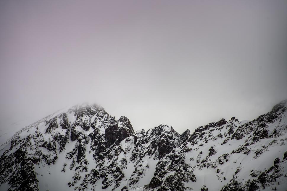 Free Image of Misty mountain peaks covered with snow and shrouded clouds. 