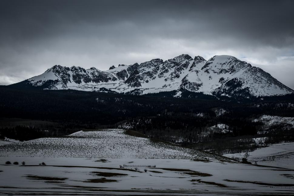 Free Image of Snowy mountain range beneath dark clouds, serene landscape. 