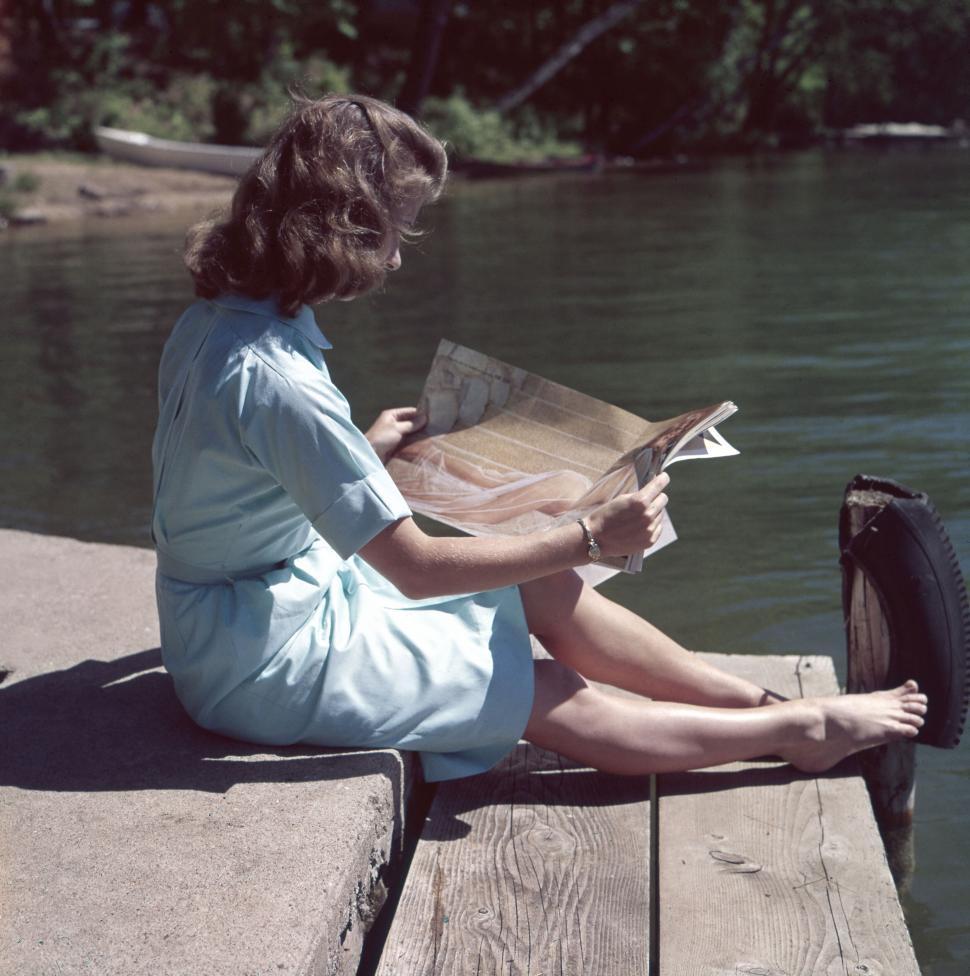 Free Image of Person reading on a wooden dock by the calm riverside. 