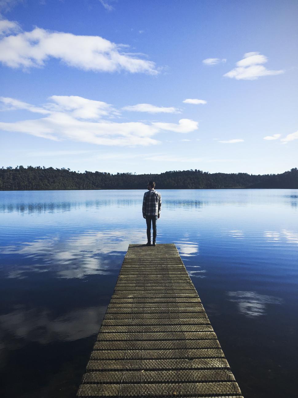 Free Image of Person standing on dock looking at calm lake and sky. 