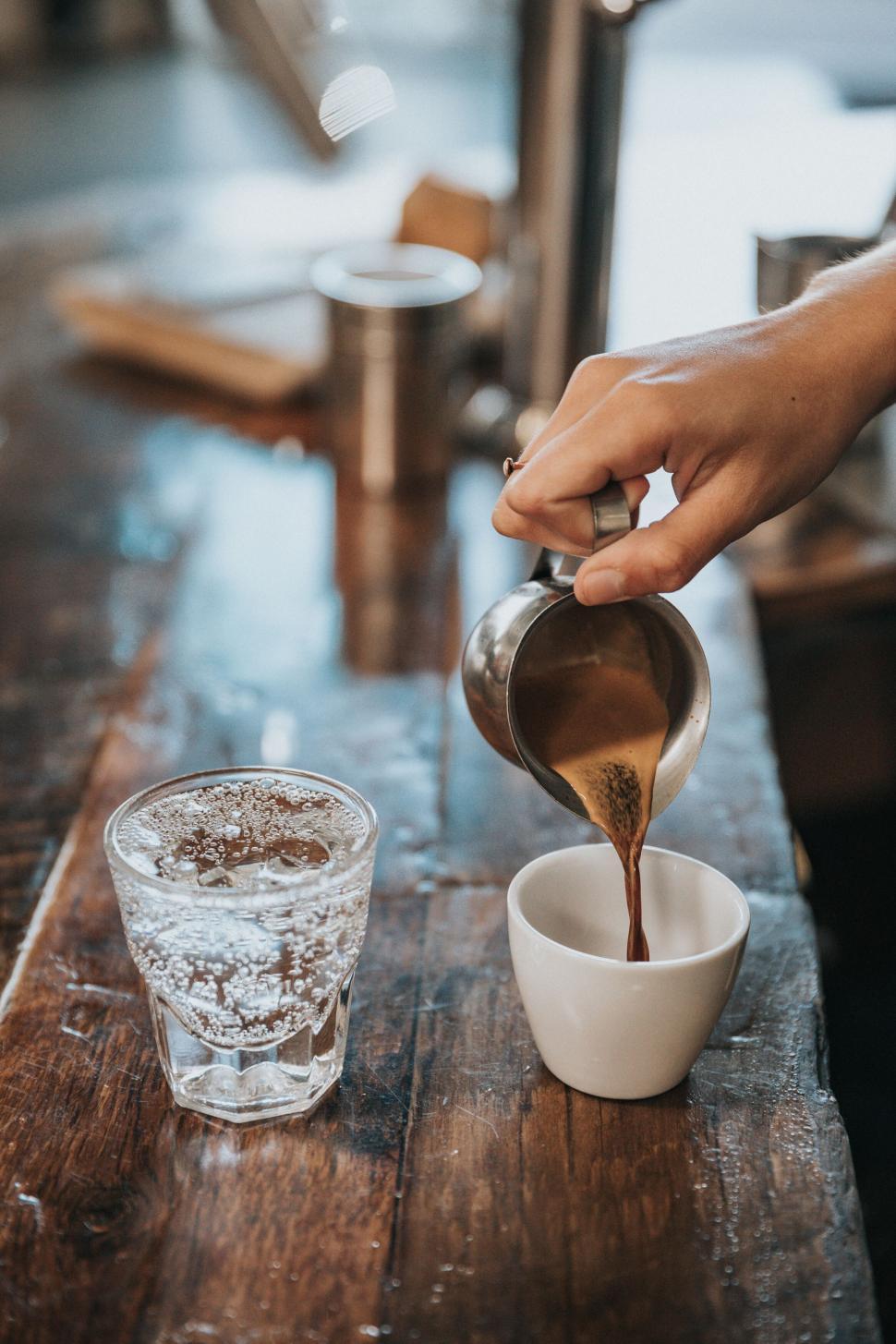 Free Image of Hand pouring freshly brewed coffee into a white cup. 