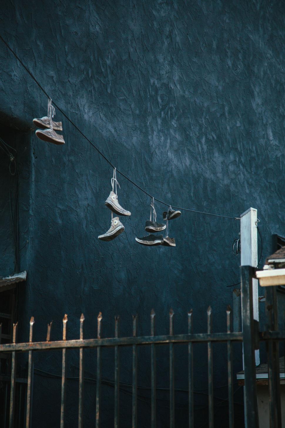 Free Image of Multiple sneakers hanging on a power line against wall. 
