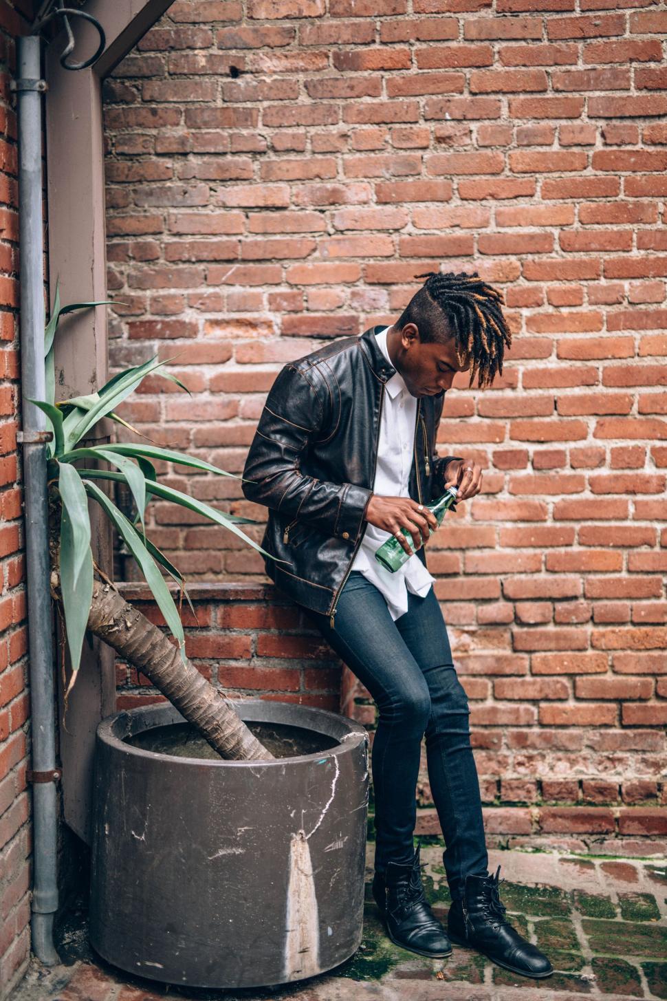 Free Image of Man in black leather jacket stands in brick alleyway corner. 
