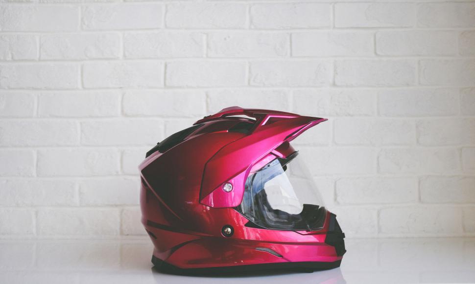 Free Image of Pink motorcycle helmet against white brick wall 