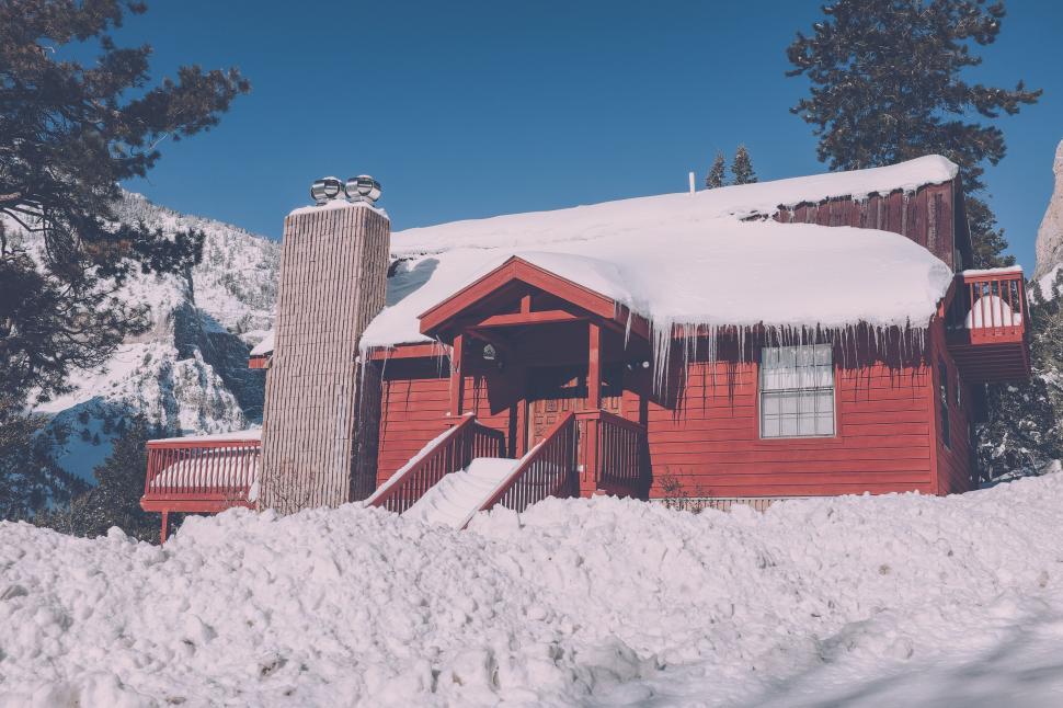 Free Image of Red cabin covered in snow with clear blue sky above 
