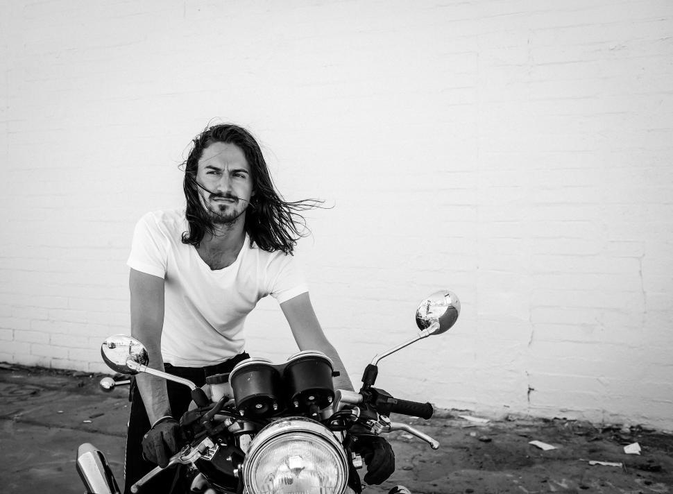 Free Image of Man with long hair sits on motorcycle in black and white. 