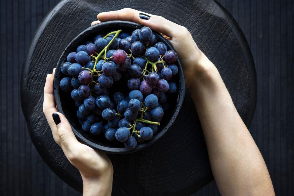 Free Image of Hands holding a bowl of ripe grapes on a black background 