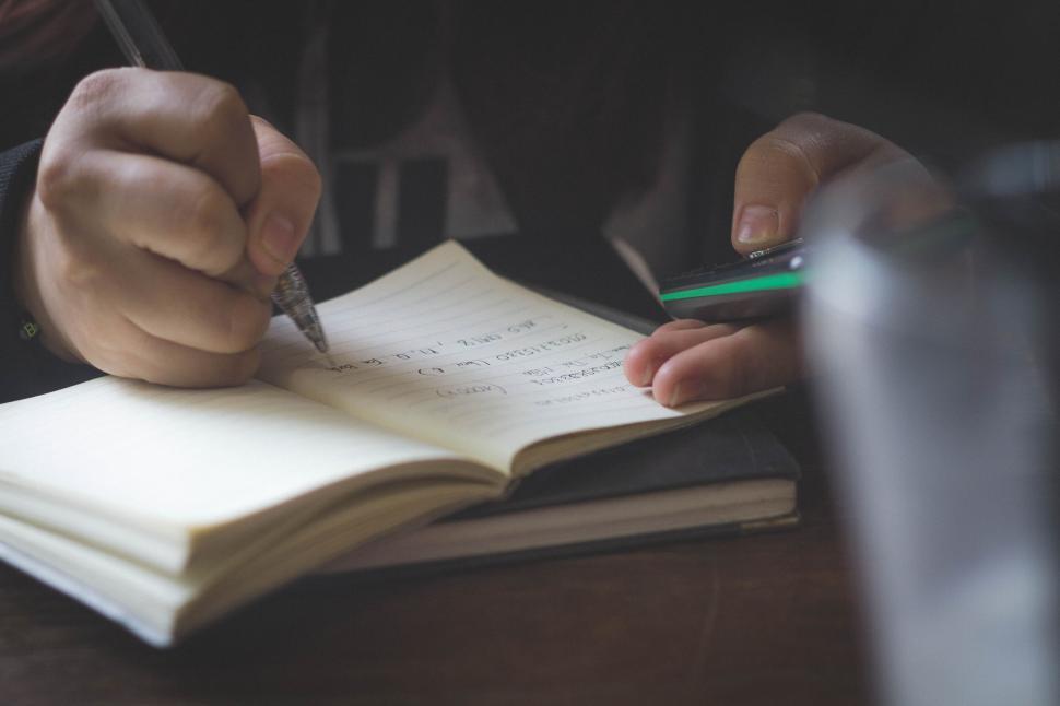 Free Image of Person writing notes with phone on table beside them 