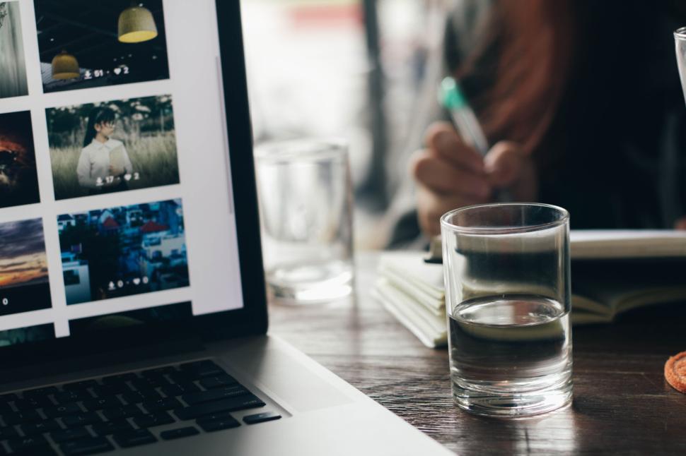 Free Image of Laptop with images and person writing in notebook. 