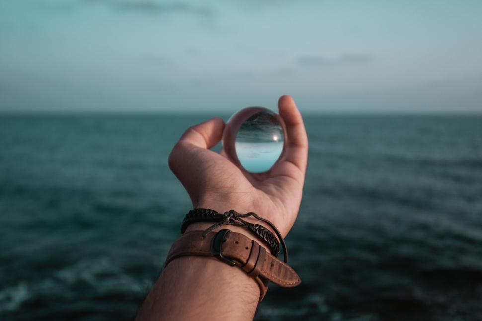 Free Image of Person holding crystal ball against ocean horizon. 