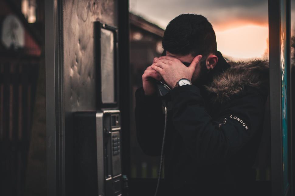 Free Image of Man in phone booth with thoughtful expression at sunset 