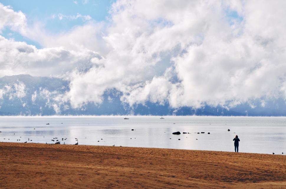 Free Image of Person walking on beach with clouds over the water. 