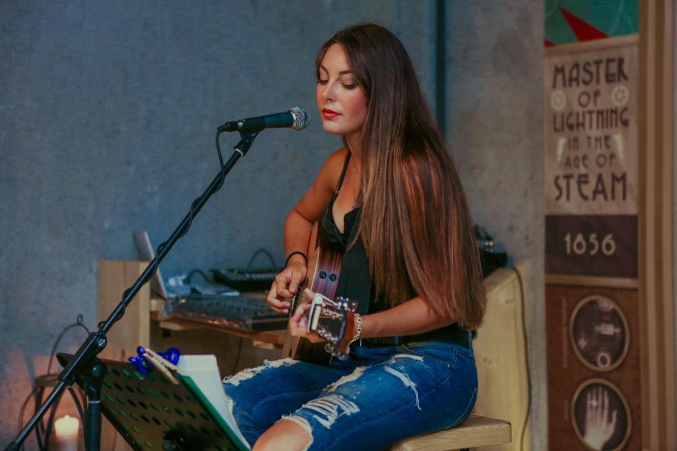 Free Image of Woman plays guitar and sings into mic on small stage. 