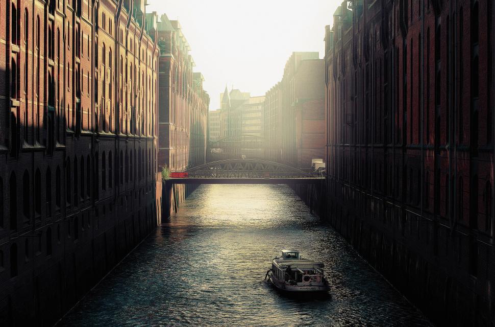 Free Image of Boat sails through canal lined with historic brick buildings. 