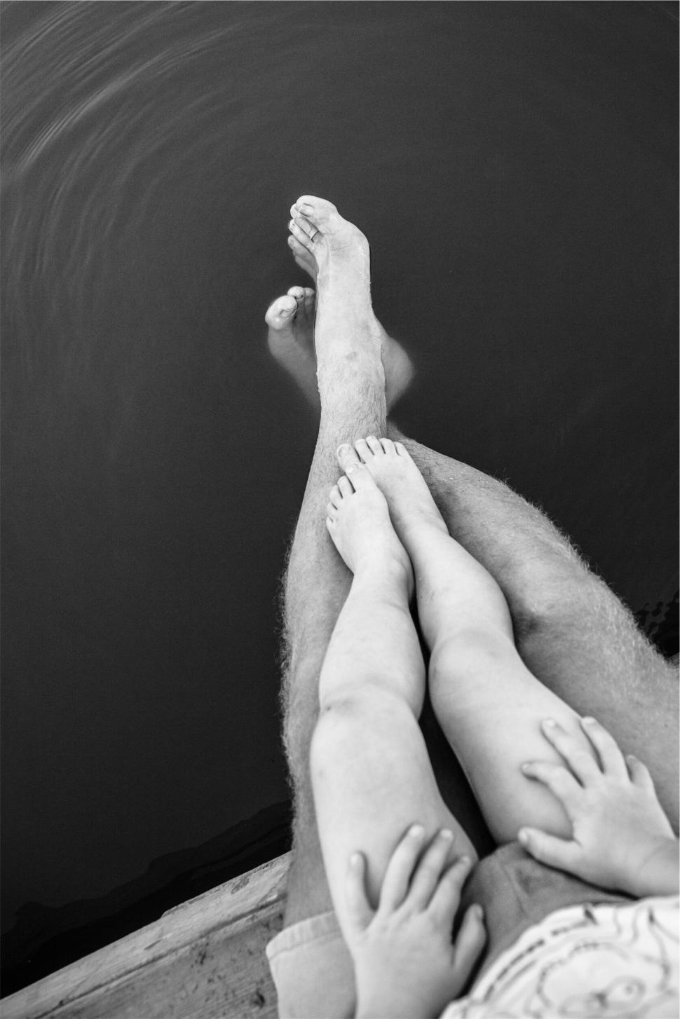 Free Image of Adult and child legs dipped in water on wooden dock. 