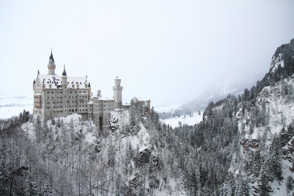 Free Image of Snowy castle on mountain surrounded by forest landscape. 