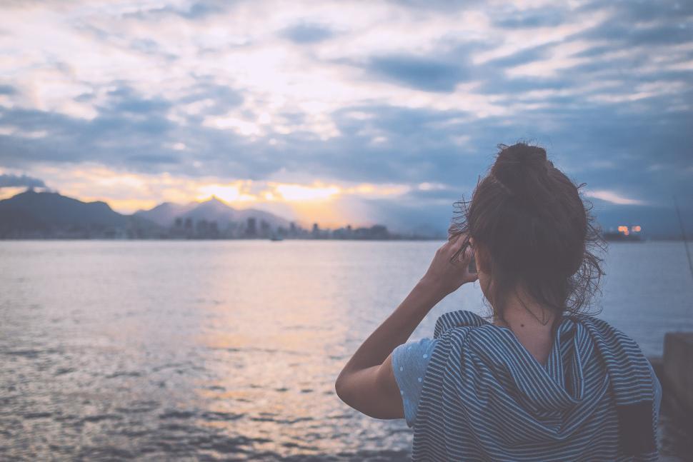 Free Image of Woman taking a photo of the ocean at sunset 