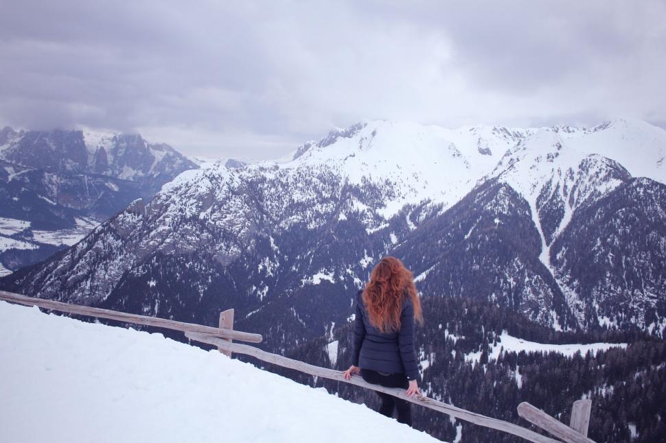 Free Image of Person sits on a fence overlooking snowy mountain range. 