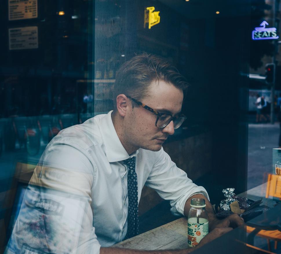 Free Image of Man behind glass window focused on laptop at cafe. 