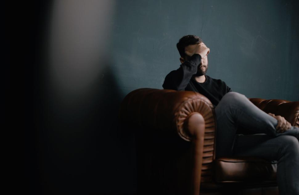 Free Image of Person sitting on a brown leather couch pondering 