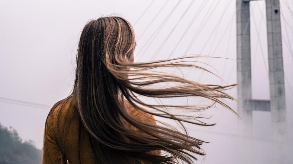 Free Image of Woman standing in front of a foggy bridge with hair blowing. 
