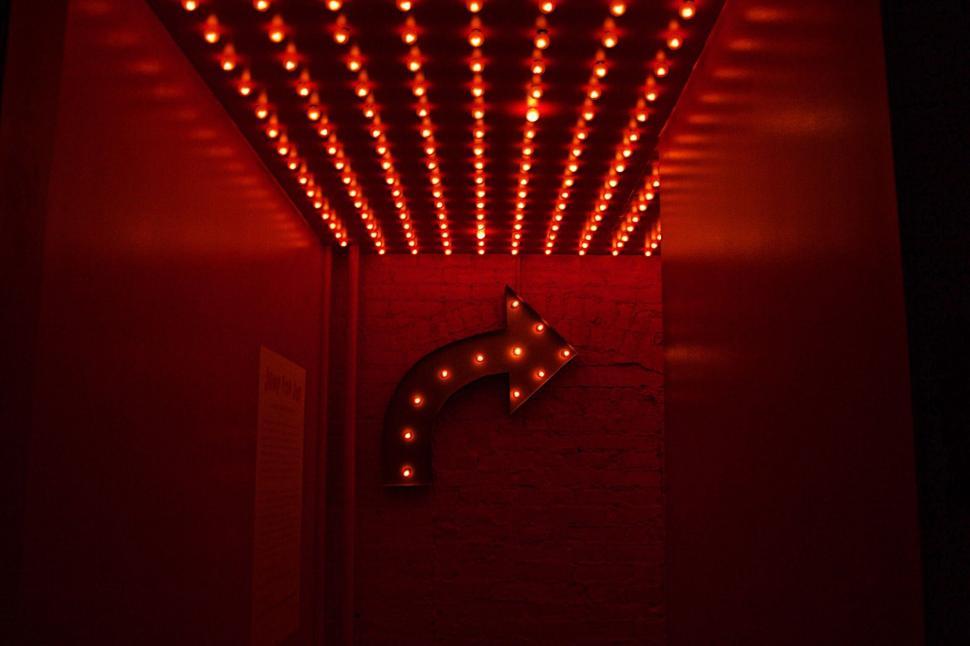 Free Image of Illuminated arrow sign in a dark room with red lights. 