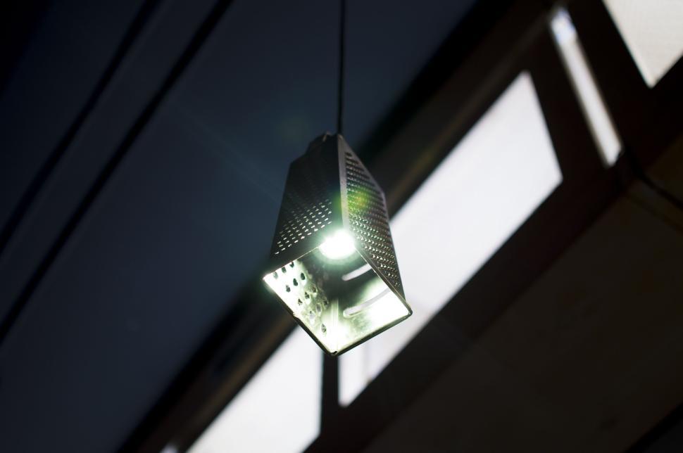 Free Image of Hanging grater lamp illuminated against dark background 