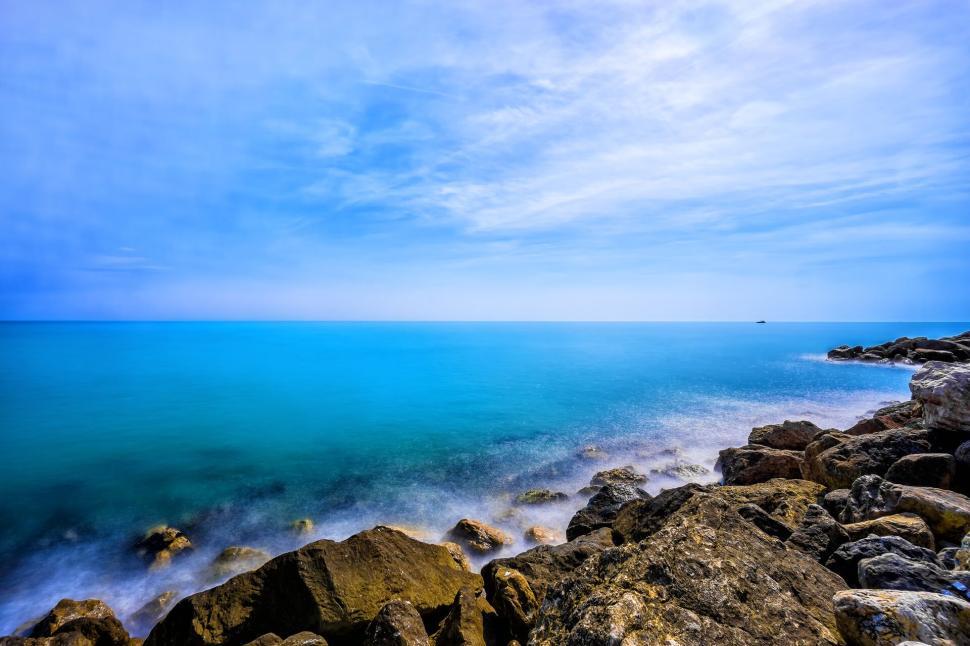 Free Image of Rocky coastline with blue waters under a clear blue sky 