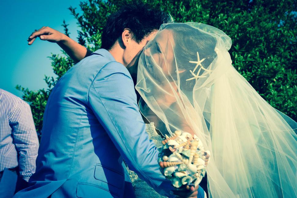 Free Image of Couple kissing at wedding with veil and bouquet 