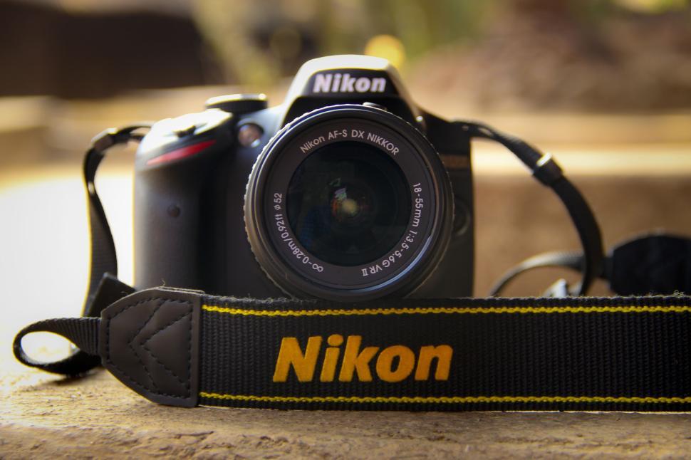 Free Image of Nikon DSLR camera with strap on a brown surface. 