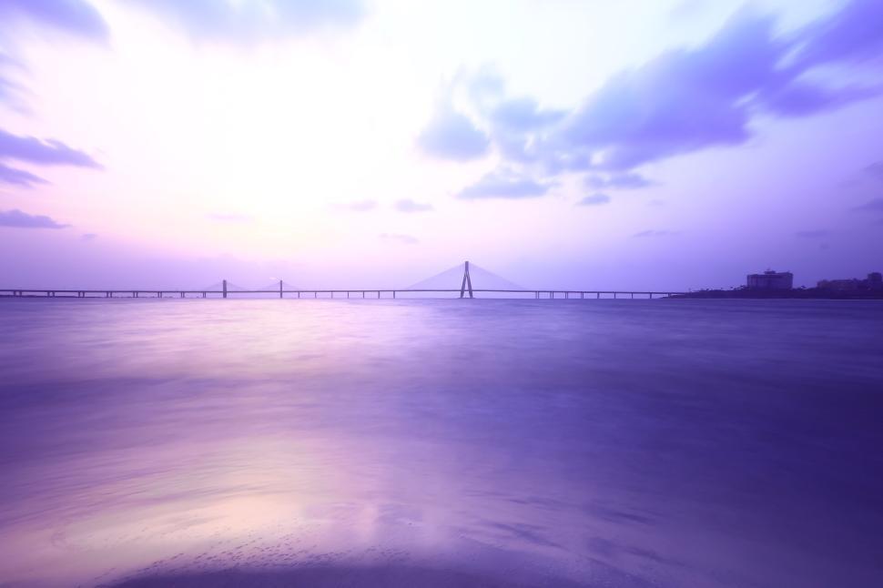 Free Image of Vibrant sunset over the sea with a distant bridge view 