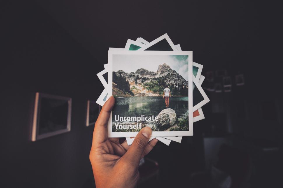 Free Image of Hand holds photos reading  Uncomplicate Yourself  on top. 