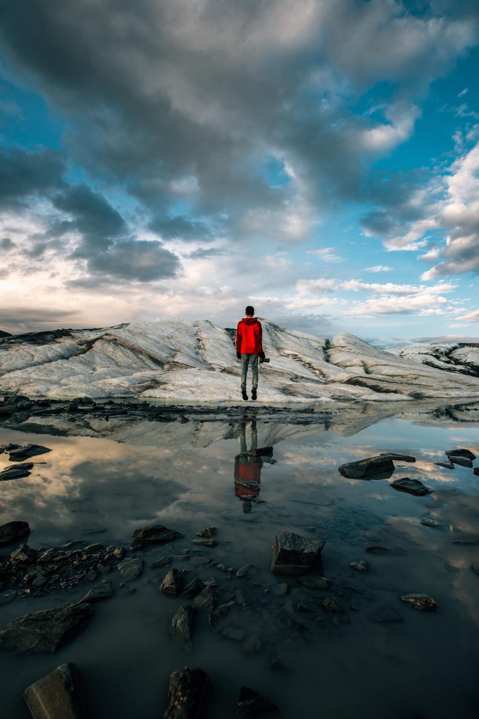 Free Image of Person in red jacket standing on rocks near icy landscape. 
