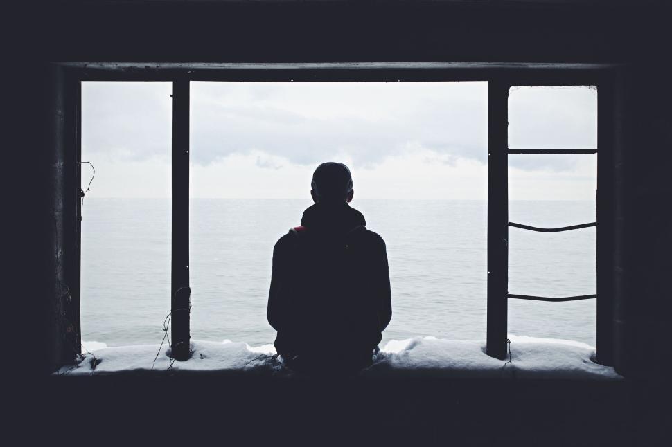 Free Image of Silhouette of a person gazing at ocean from a window. 
