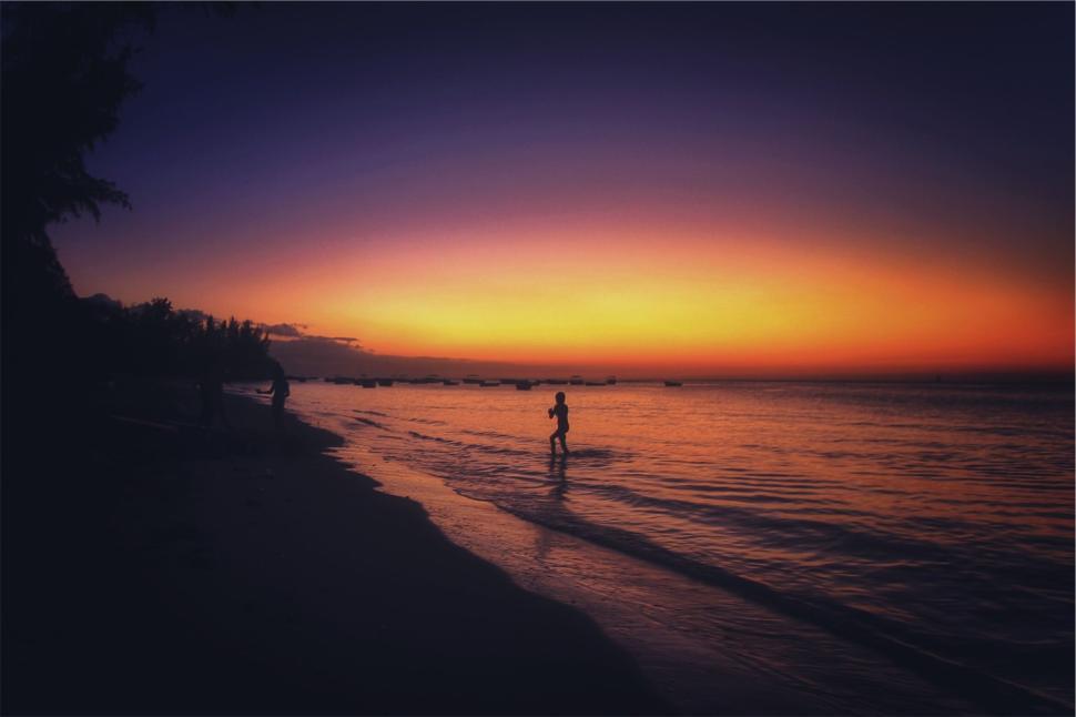 Free Image of Silhouetted person walking on the beach at sunset time 