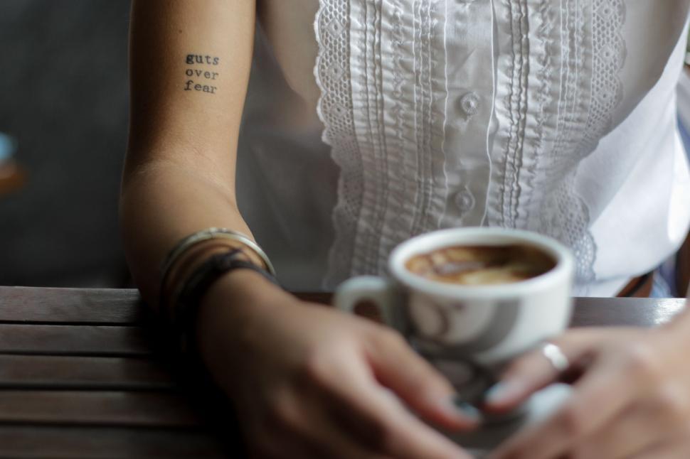 Free Image of Woman with tattoo and coffee cup on wooden table 