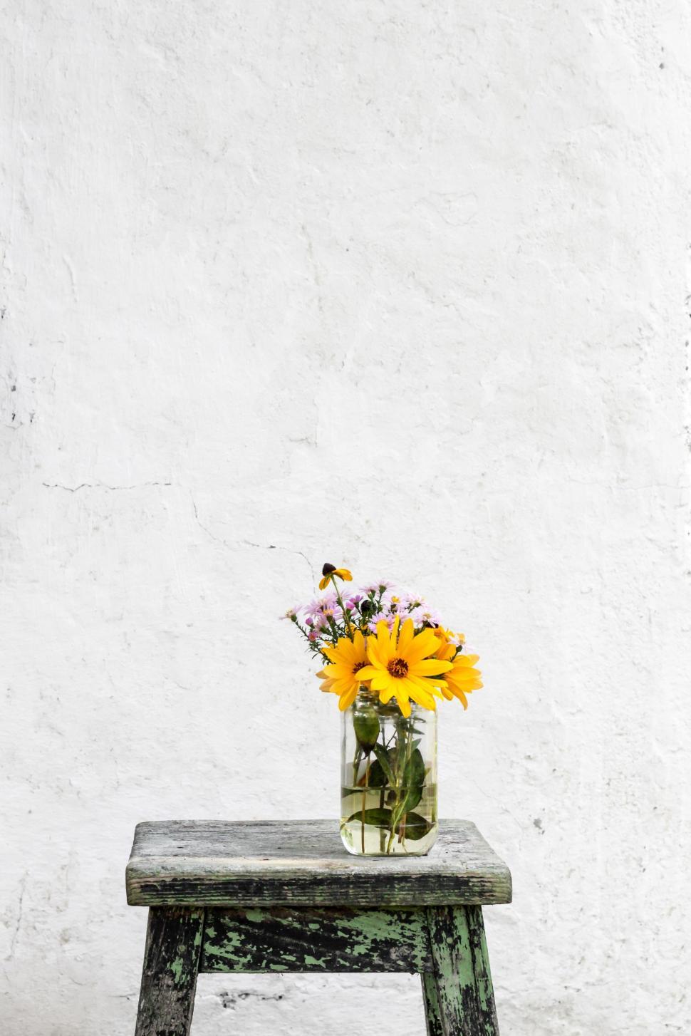 Free Image of Yellow flowers in vase on rustic wooden stool background 