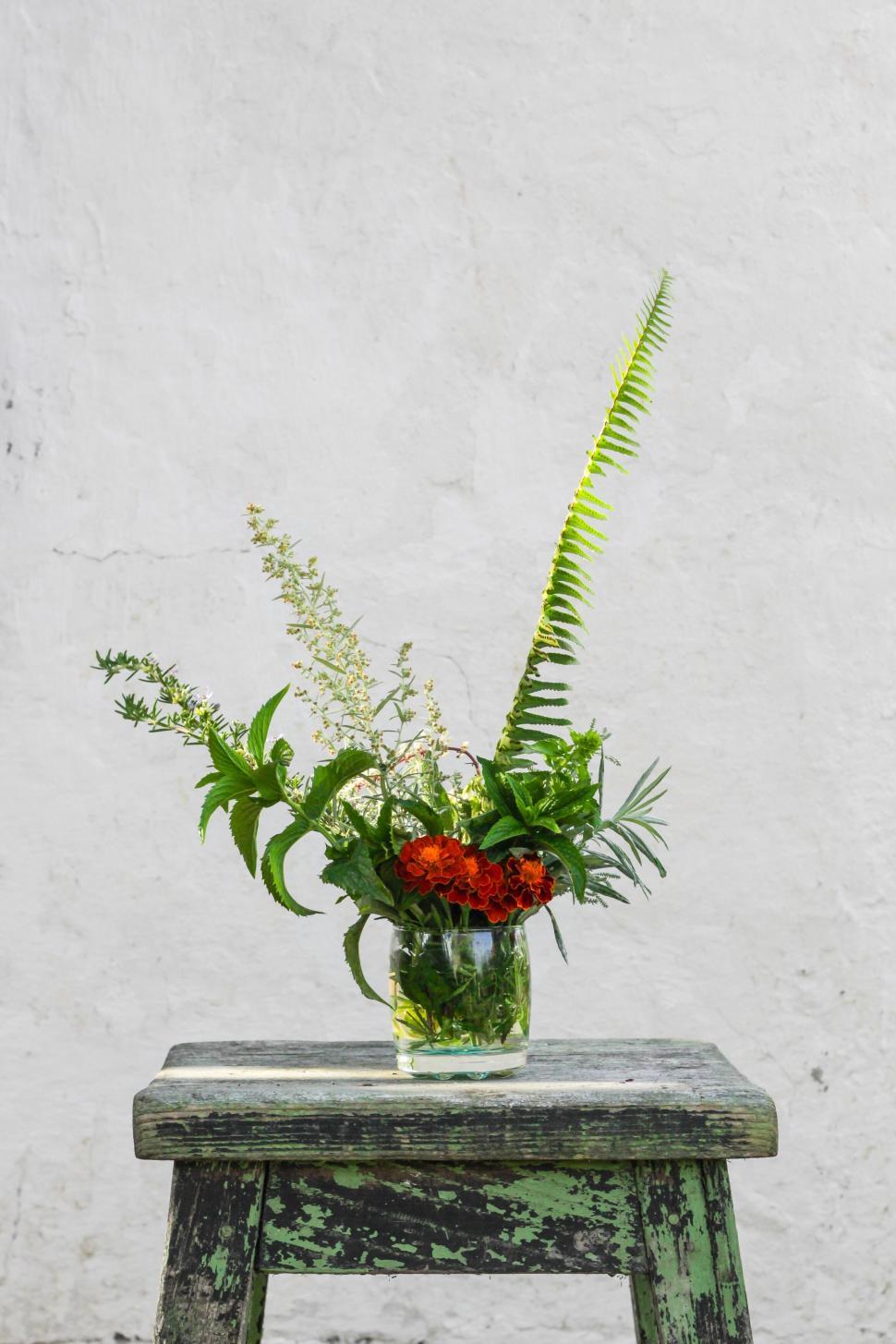 Free Image of Floral and green plant arrangement in glass vase on stool 