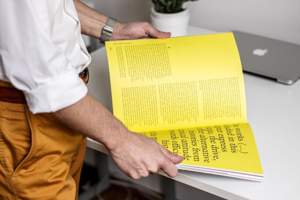 Free Image of Person holding open yellow book while standing indoors. 